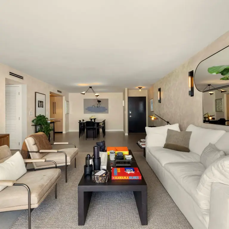 Open-plan living room with linen sofa, lounge chairs and dark wood coffee table facing the dining area at Costa Residence