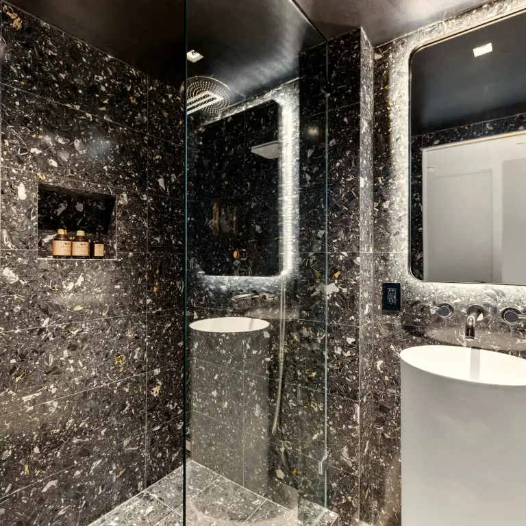 Walk-in shower and pedestal vanity clad in black terrazzo-look tile at Costa Residence