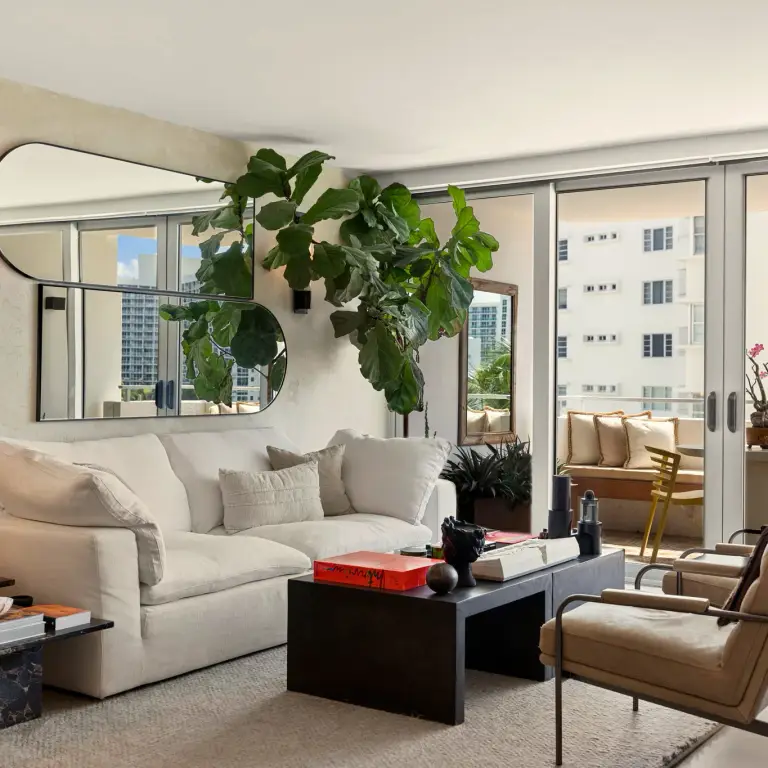Living room with linen sofa, oblong mirror and fiddle-leaf fig beside sliding doors to the balcony at Costa Residence