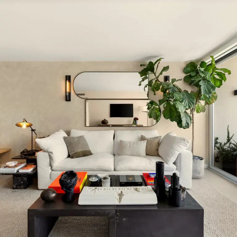 Sofa beneath an oblong mirror flanked by wall sconces at Costa Residence