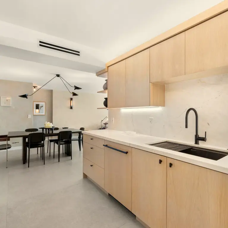Kitchen with light oak flat-panel cabinetry, marble backsplash and black fixtures at Costa Residence