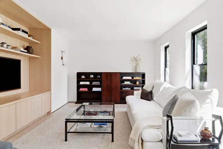 Living room with a built-in oak media wall, white sofa, glass coffee table and rosewood bookcase at the Farmstead