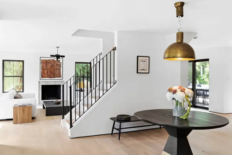 Entry dining area with a round dark-wood pedestal table, brass dome pendant and black steel stair rail at the Farmstead