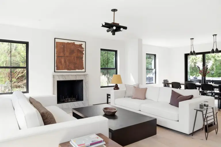 Living room with white sofas, a black coffee table and a marble fireplace beneath black-trimmed windows at the Farmstead