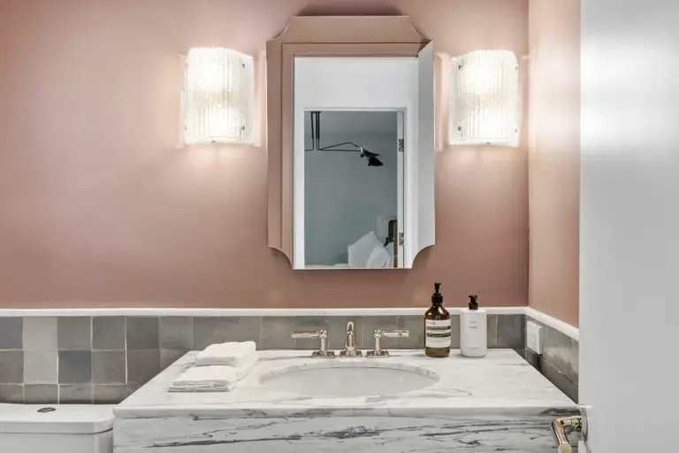 Powder room with pink plaster walls, an arched mirror and fluted glass sconces over a marble vanity at the Farmstead