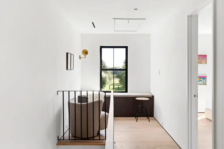 Upstairs landing with a built-in walnut window bench, brass sconce and bouclé chair at the Farmstead