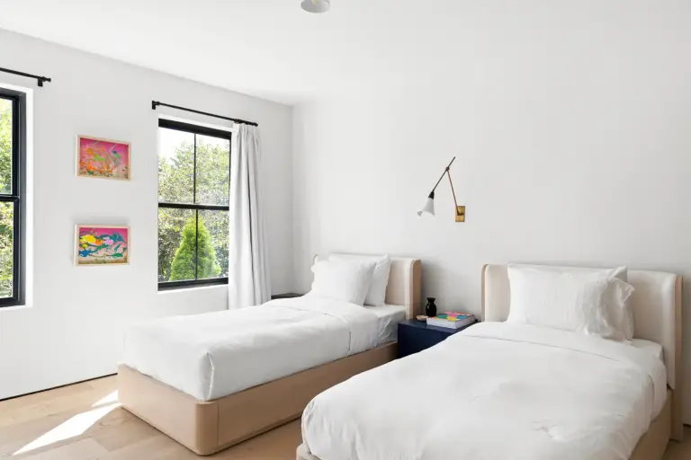 Guest bedroom with twin beds, a navy nightstand and an articulating brass sconce at the Farmstead