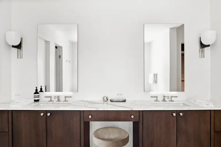 Double vanity with dark walnut cabinetry, marble counters, twin mirrors and globe sconces at the Farmstead