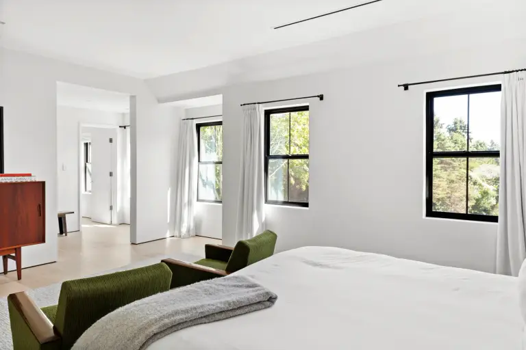 Bedroom with green corduroy lounge chairs, a rosewood credenza and tree views at the Farmstead