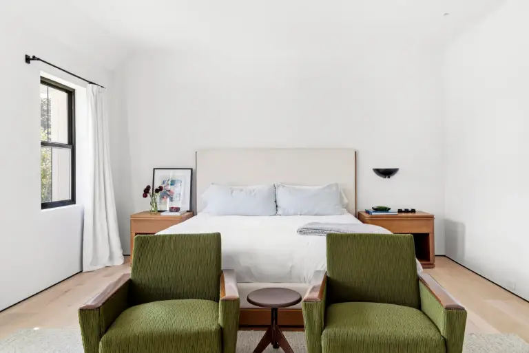 Bedroom with an upholstered bed between walnut nightstands and green corduroy chairs at the foot at the Farmstead