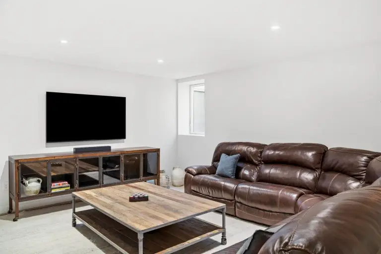 Basement media room with leather recliner sofas and a wall-mounted TV over an industrial wood console at the Farmstead