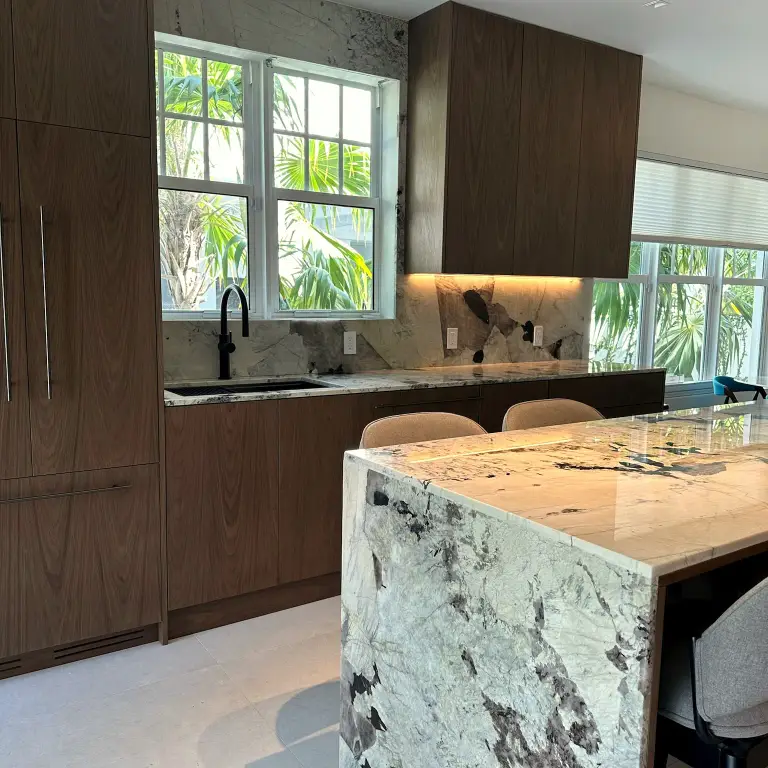 Kitchen with walnut flat-panel cabinetry, marble waterfall island and black faucet at Feit Residence