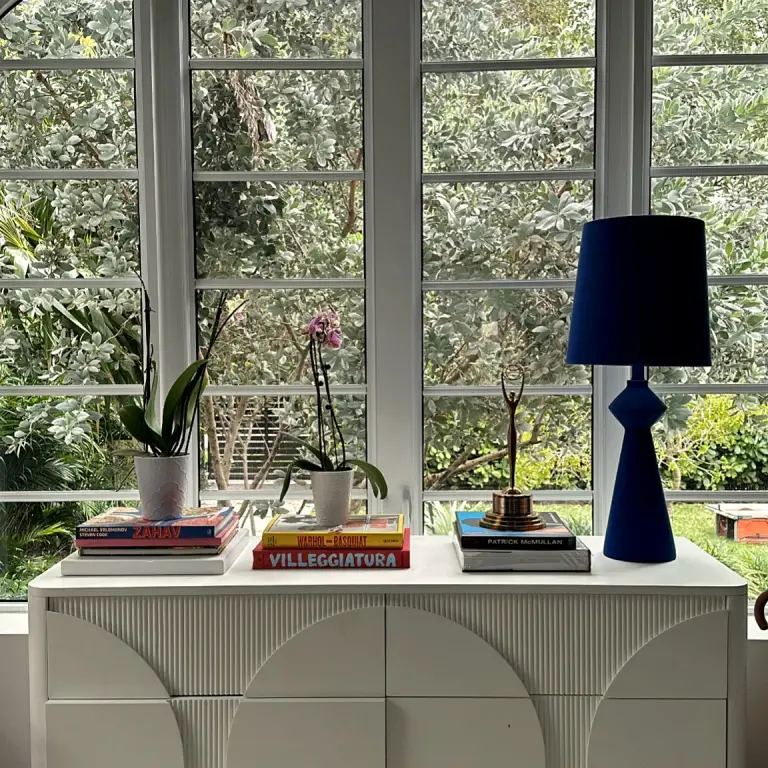 Window-side credenza styled with coffee-table books, orchids and a navy lamp at Feit Residence