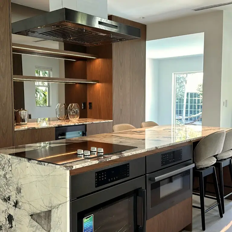 Kitchen island with induction cooktop, built-in ovens and stainless hood before a walnut wet bar at Feit Residence