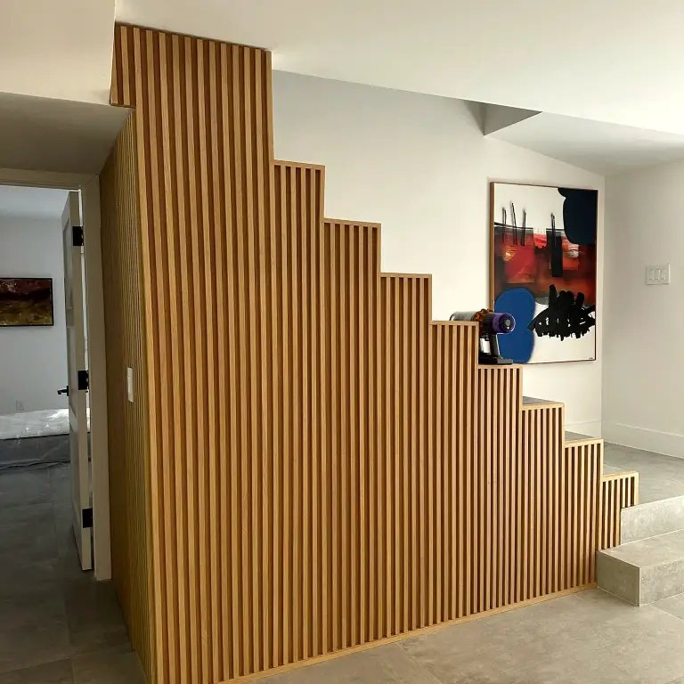 Hallway with stepped fluted-oak millwork wall and abstract artwork at La Gorce Residence