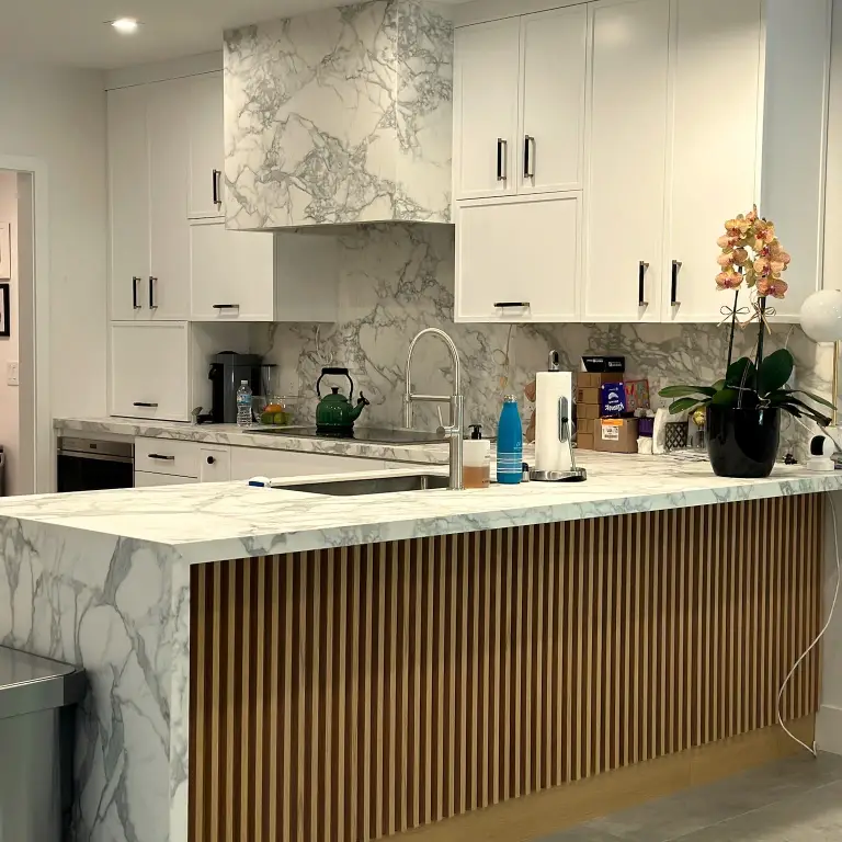 Kitchen with marble waterfall island over fluted wood panels and a marble backsplash at La Gorce Residence