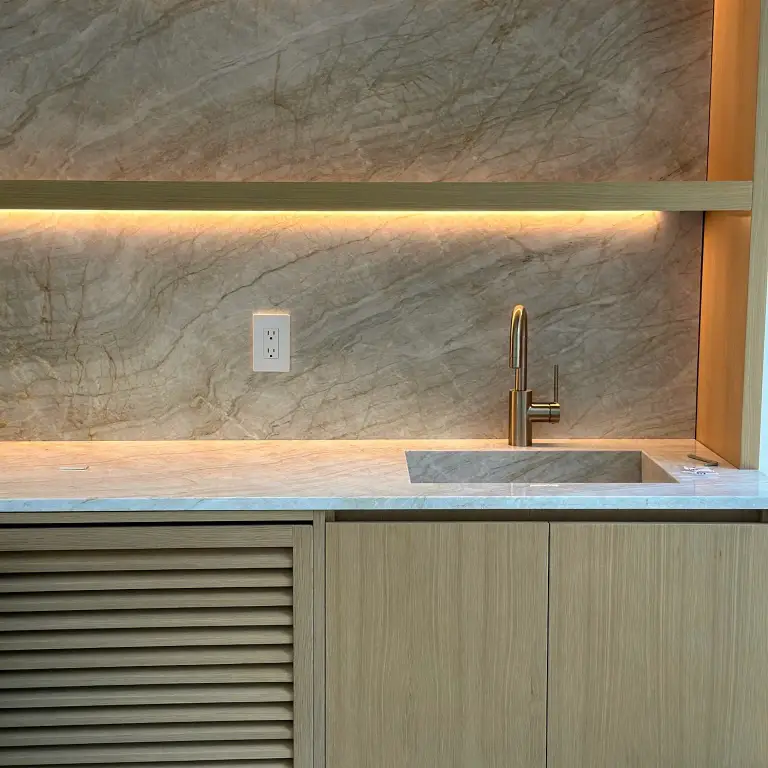 Wet bar with marble backsplash, integrated stone sink and brushed brass faucet at La Gorce Residence
