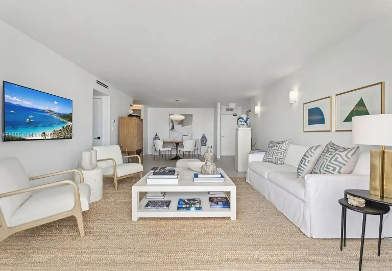 Living room with wall-mounted TV, slipcovered sofa and cane lounge chairs on a jute rug at Silver Residence
