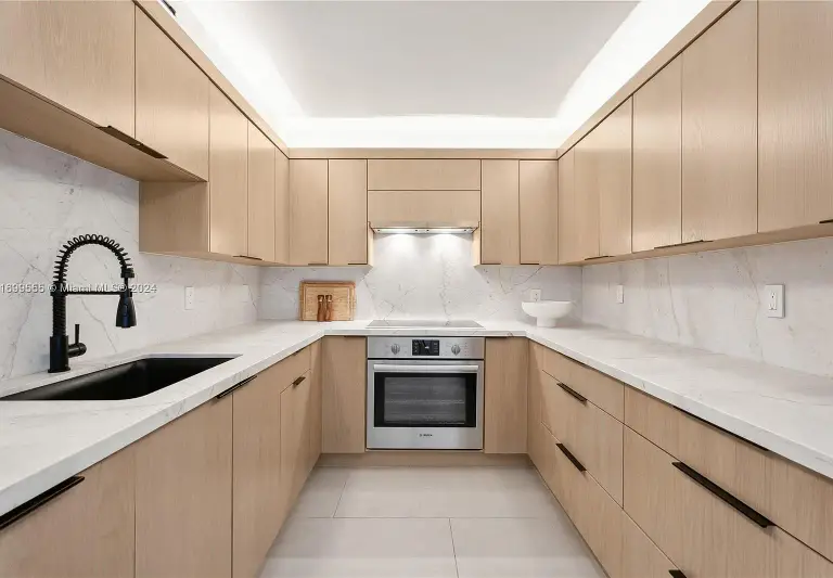 Galley kitchen with white oak flat-panel cabinets, marble counters and a black gooseneck faucet at Silver Residence