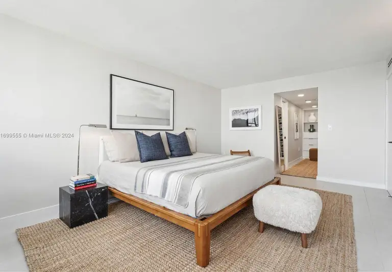 Primary bedroom with platform bed, black marble nightstand and shearling ottoman on a jute rug at Silver Residence