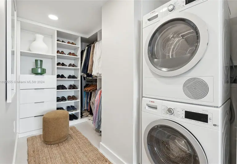 Walk-in closet with open shelving, clothing rails and a stacked Bosch washer and dryer at Silver Residence