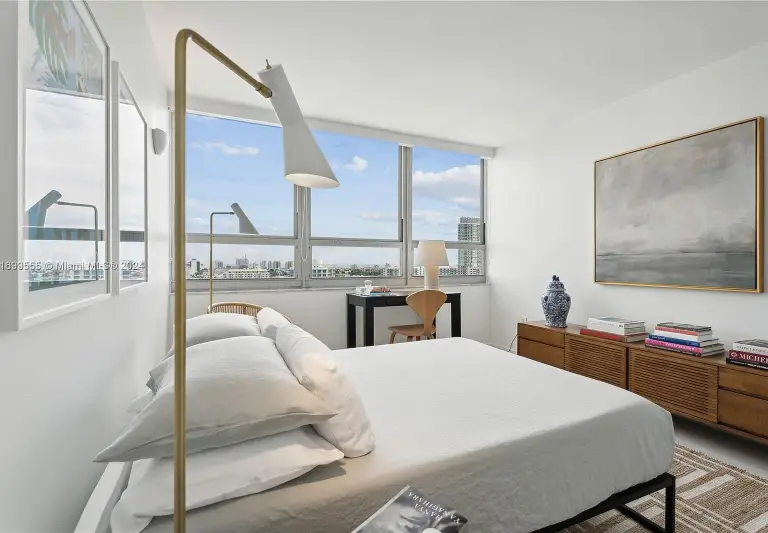 Guest bedroom with a brass floor lamp, walnut credenza and city views through bay windows at Silver Residence