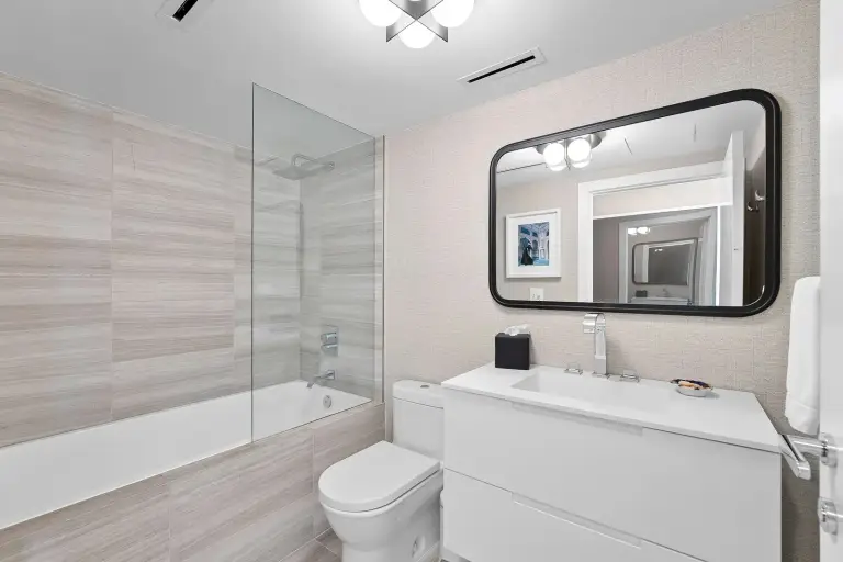Bathroom with a white vanity, black-framed mirror and glass shower over a tub at Starr DeVos Condo