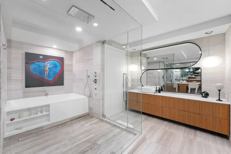 Bathroom with a floating walnut vanity, vessel sink and freestanding tub beside a glass shower at Starr DeVos Condo