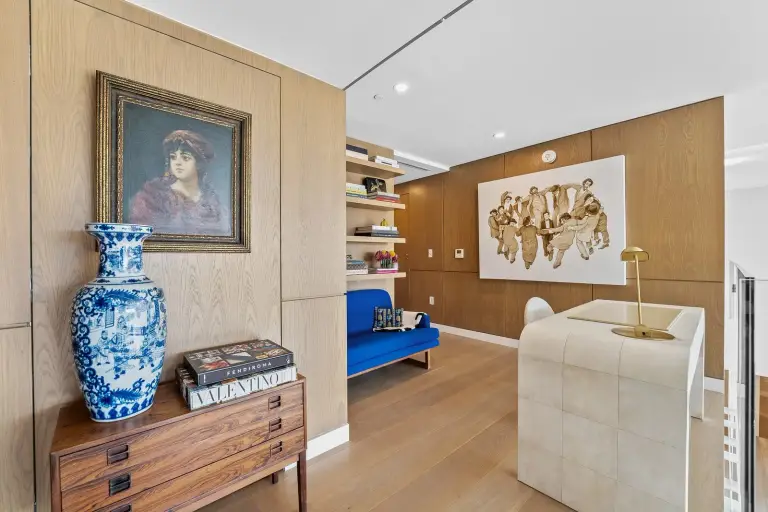 Hallway study with oak paneling, a framed portrait and coffee-table books on a rosewood dresser at Starr DeVos Condo