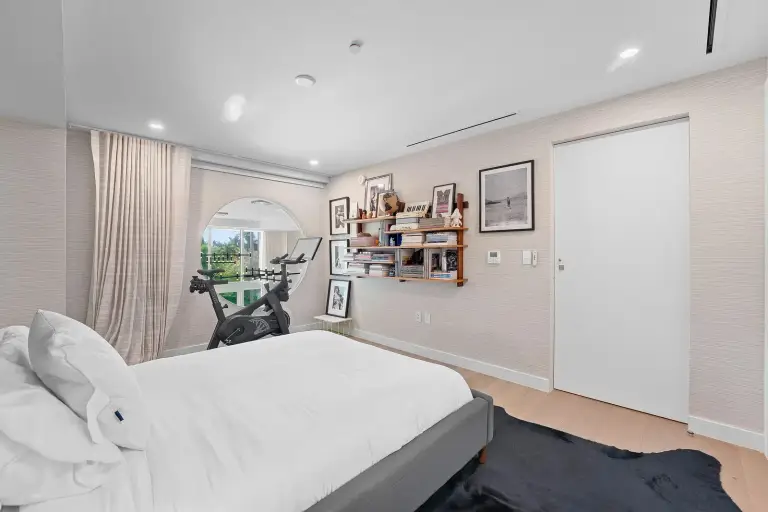 Bedroom office with a Peloton bike, round mirror and bookshelf on grasscloth walls at Starr DeVos Condo