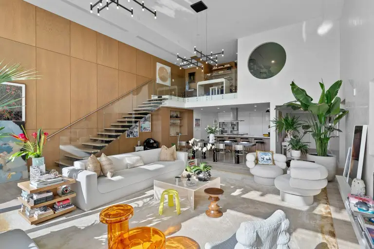 Double-height living room with a floating staircase and glass balustrade at Starr DeVos Condo
