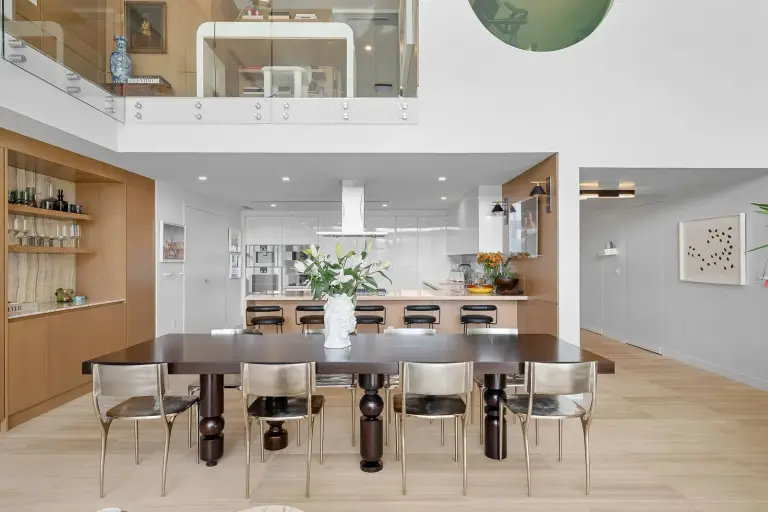Dining space with a turned-leg wood table beneath the mezzanine, open to the kitchen at Starr DeVos Condo