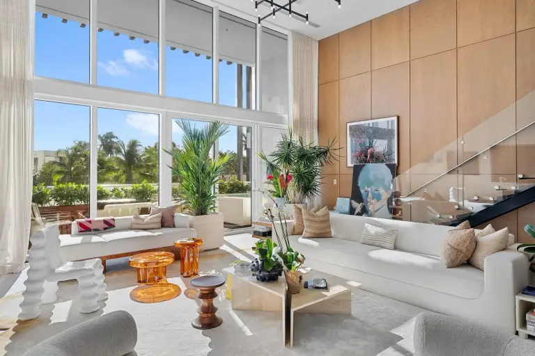 Living room with a white sofa, sculptural chair and large botanical artwork against a wood panel wall at Starr DeVos Condo