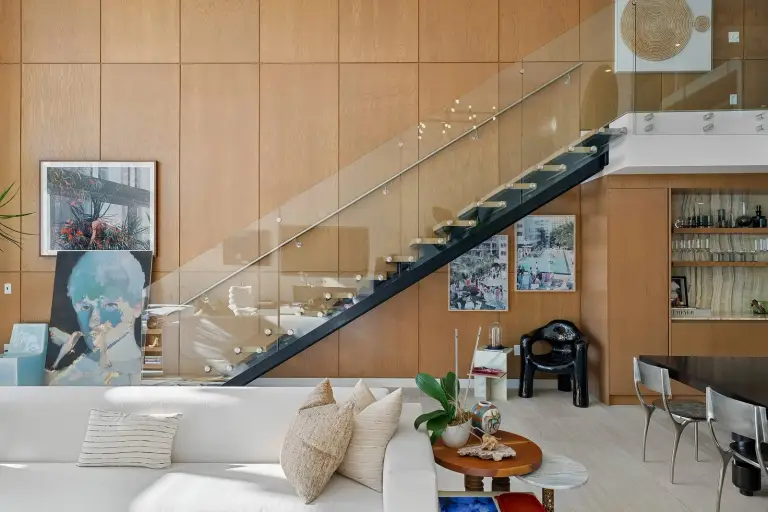 Floating staircase with a glass rail and steel stringer above an onyx-backed wet bar at Starr DeVos Condo