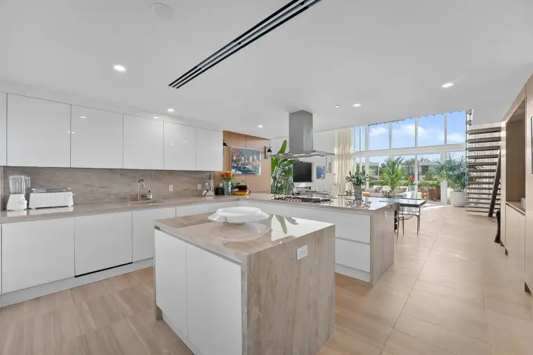 Kitchen with white lacquer cabinets, travertine counters and a stair up to the mezzanine at Starr DeVos Condo