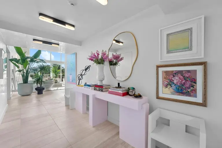 Gallery hallway with a lacquered console, organic-shaped mirror and framed artwork against marble walls at Starr DeVos Condo