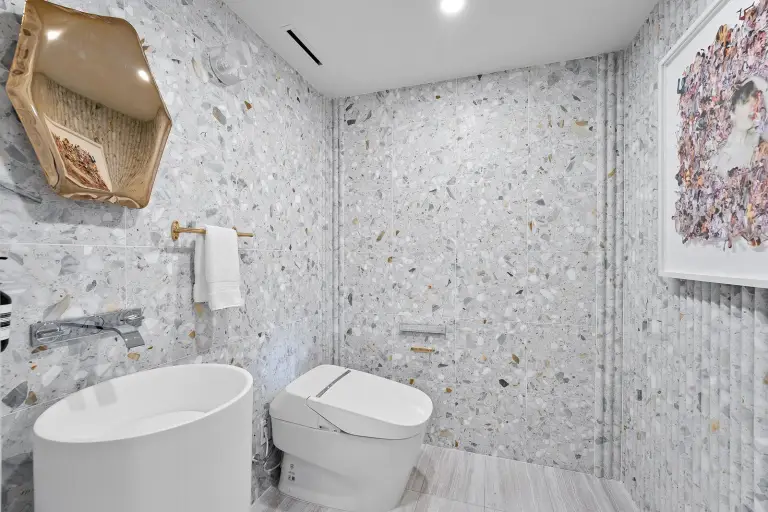 Powder room with terrazzo tile walls, a sculptural gold mirror and a pedestal sink at Starr DeVos Condo